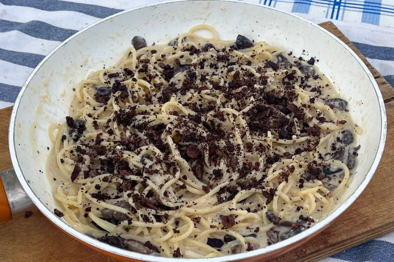 Spaghetti cremosi con olive nere e una spolverata di briciole scure, un'interpretazione audace della pasta alla cenere.