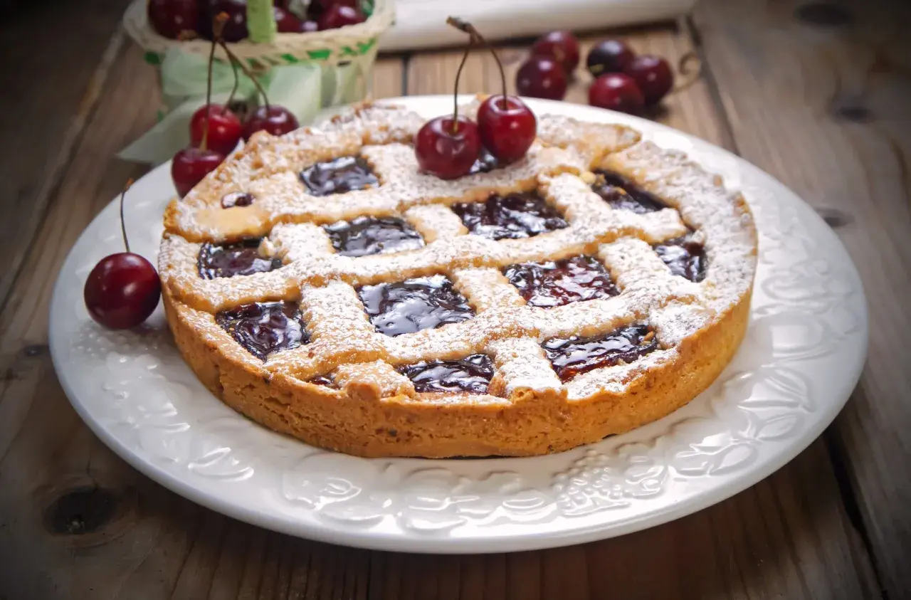 Deliziosa crostata senza burro con marmellata di ciliegie, cosparsa di zucchero a velo e decorata con ciliegie fresche.