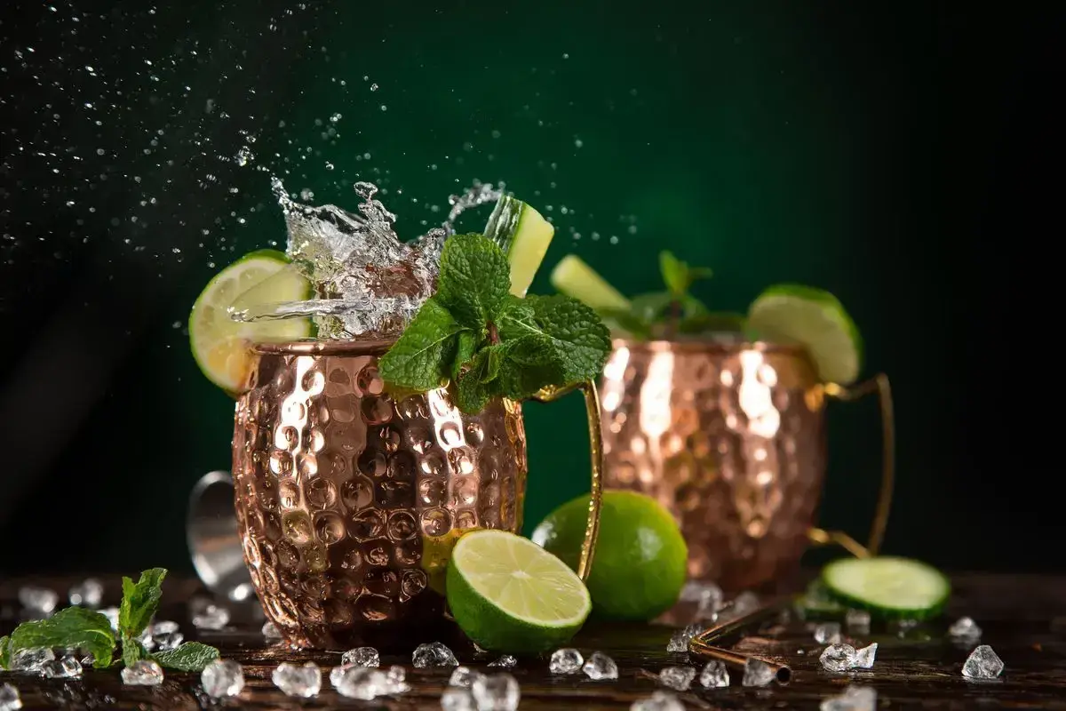 Moscow Mule ricetta: due tazze di rame con schizzi d'acqua, lime, menta e cetriolo. Fresco e dissetante.