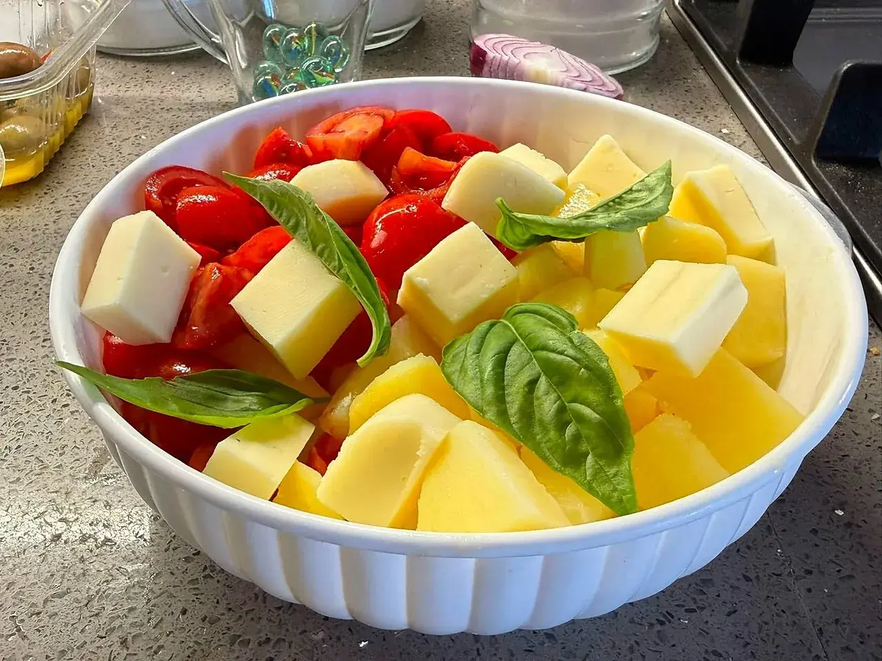 Insalata di pomodori freschi, cubetti di formaggio e foglie di basilico in una ciotola bianca.