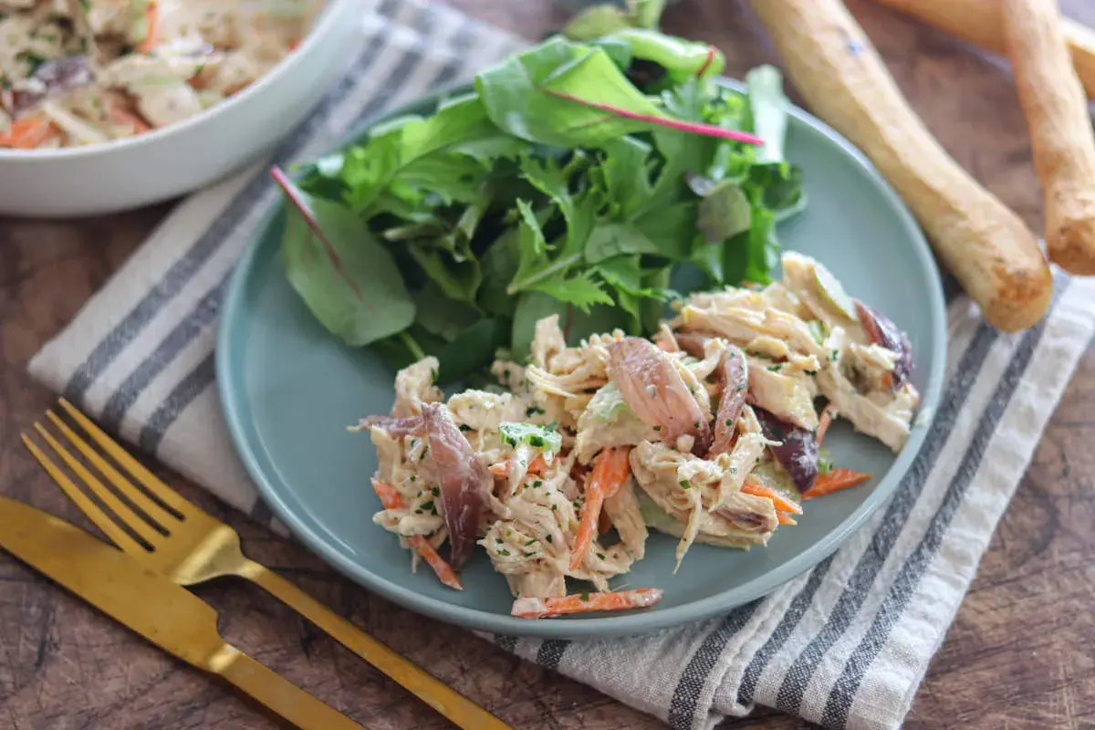 Deliziosa insalata di pollo con carote, sedano e un tocco di erbe fresche, servita con un contorno di insalata mista.