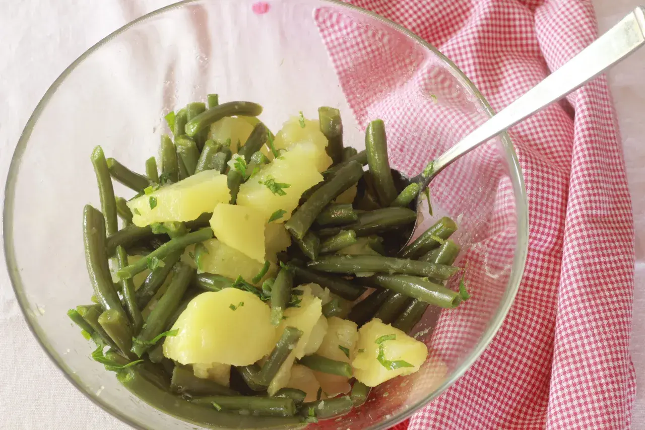 Insalata di fagiolini e patate, condita con erbe fresche, servita in una ciotola di vetro su un tovagliolo a quadretti rossi.