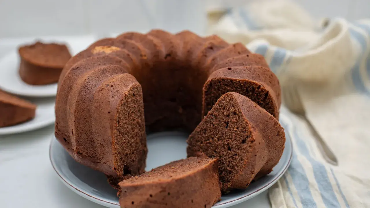 Un delizioso ciambellone al cioccolato, soffice e invitante, con una fetta tagliata che mostra la sua morbidezza.