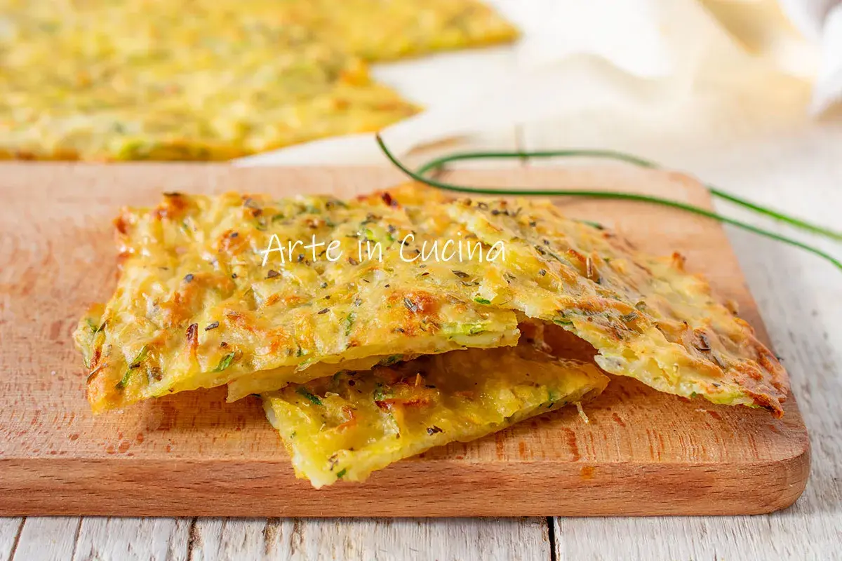 Schiacciata di zucchine dorata e croccante, condita con erbe aromatiche, servita su un tagliere di legno.