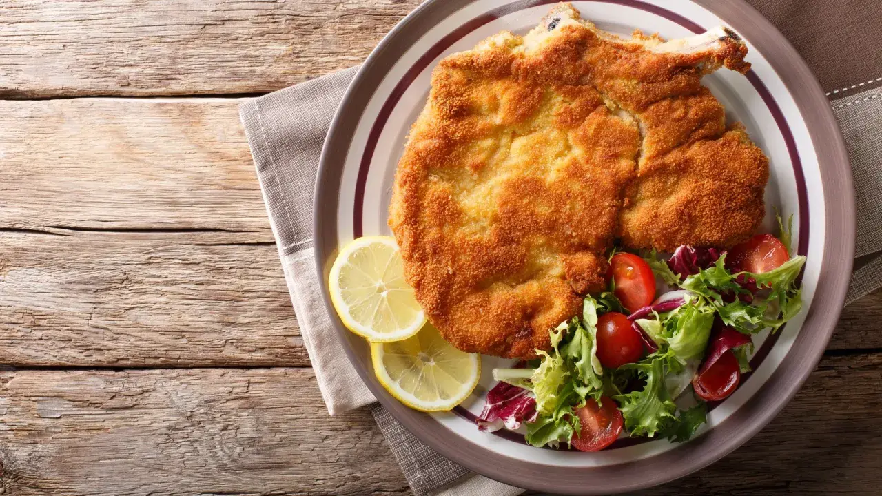 Una dorata cotoletta alla milanese, croccante e succulenta, servita con spicchi di limone e un'insalata fresca.