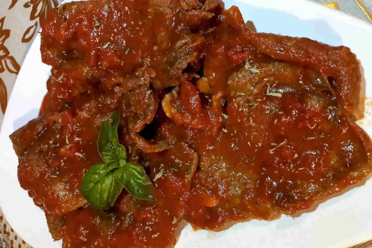 Fette di carne alla pizzaiola siciliana, ricoperte da un sugo rosso saporito e guarnite con basilico fresco.