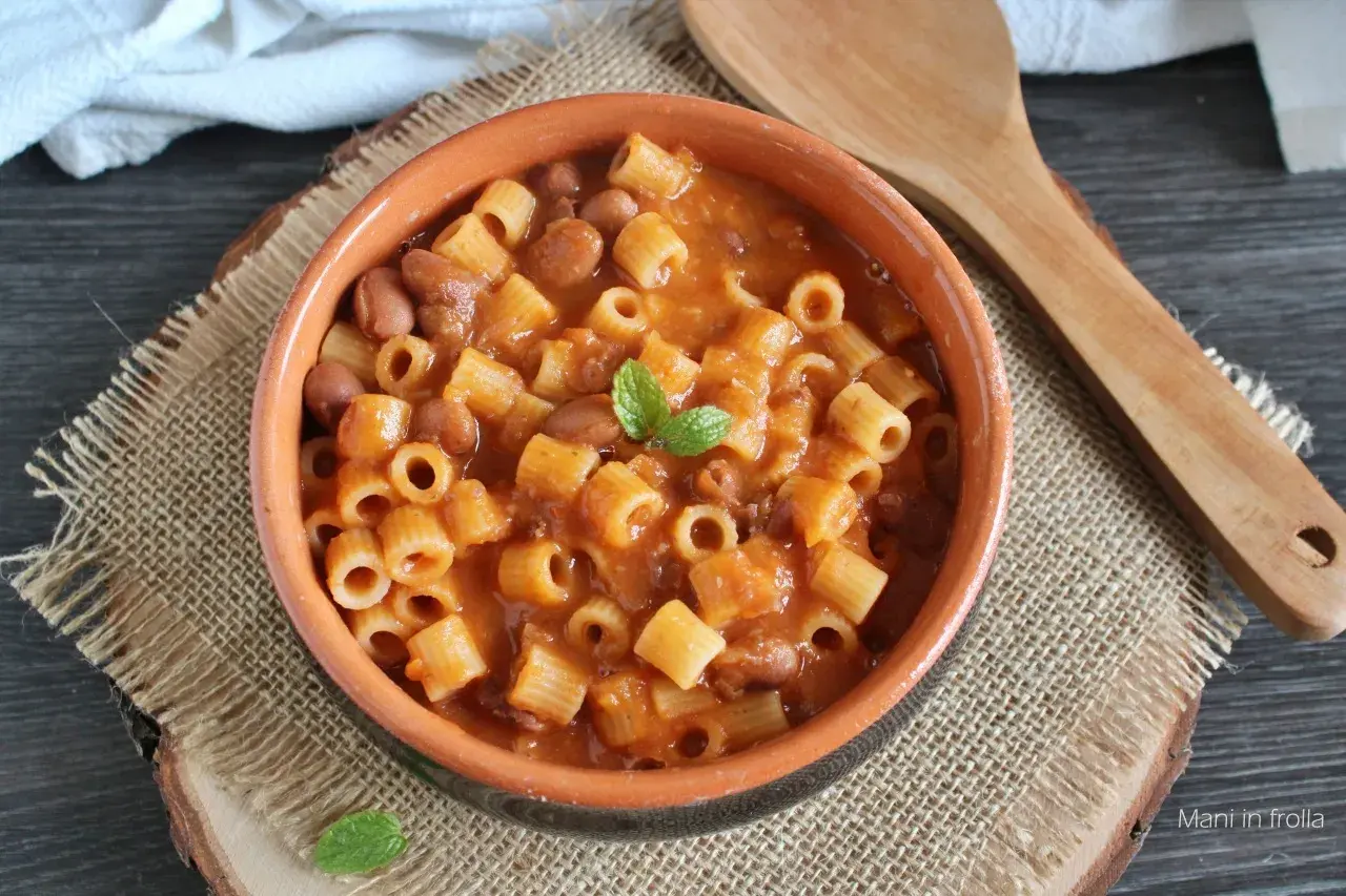 Un piatto fumante di pasta e fagioli in scatola, guarnito con menta fresca, servito in una ciotola di terracotta su una tovaglietta di juta.