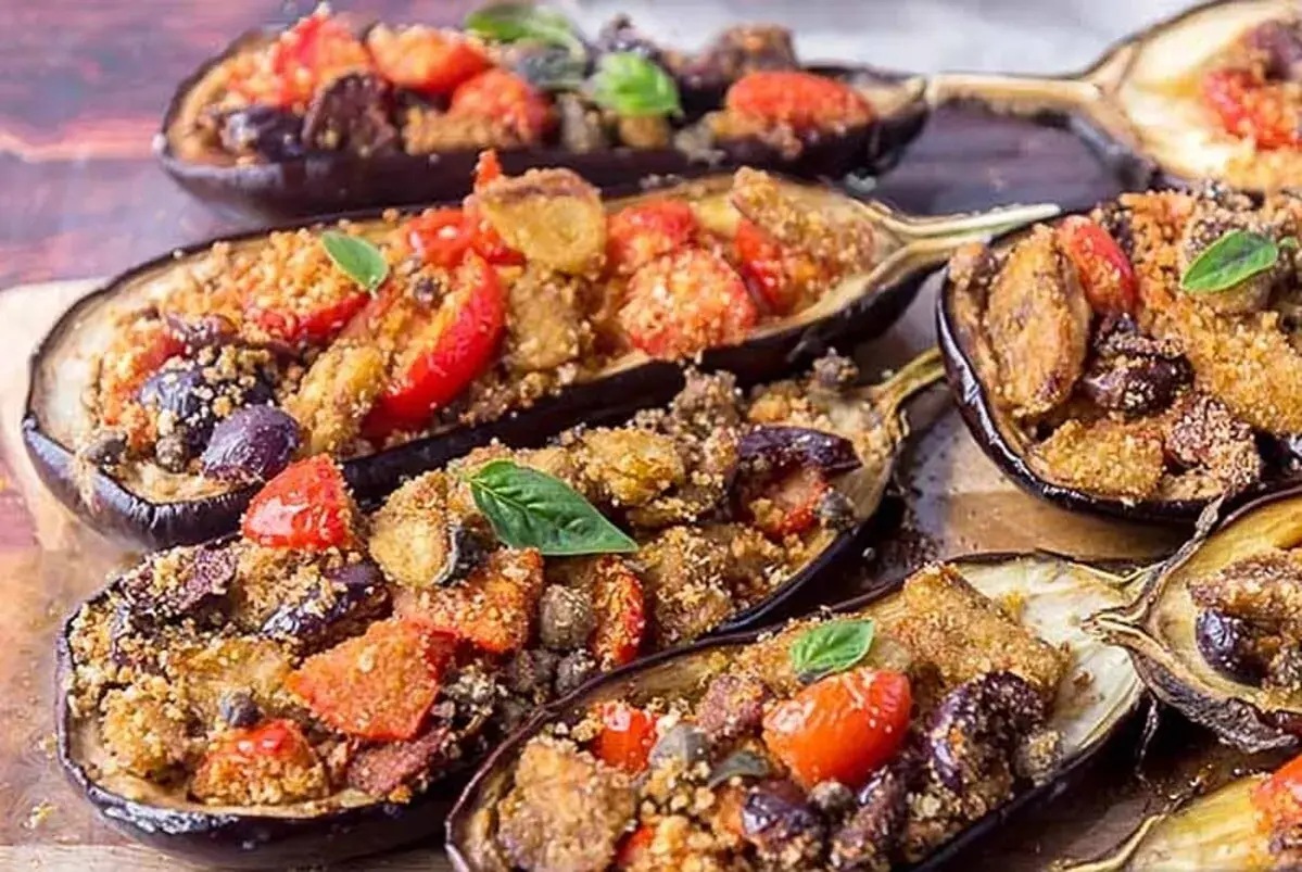 Melanzane a scarpone ripiene di pomodorini, olive e pangrattato, guarnite con basilico fresco. Un piatto saporito e invitante.