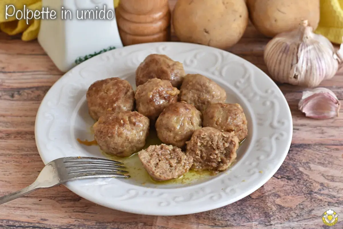 Polpette in umido succulente su un piatto bianco, con una forchetta pronta ad assaggiarle. Sullo sfondo, patate e aglio.