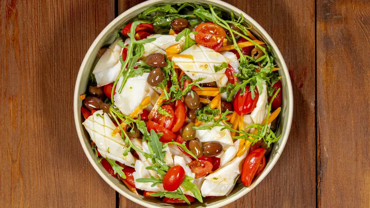 Insalata di calamari fresca con pomodorini, olive, rucola e carote julienne, un piatto estivo colorato e saporito.