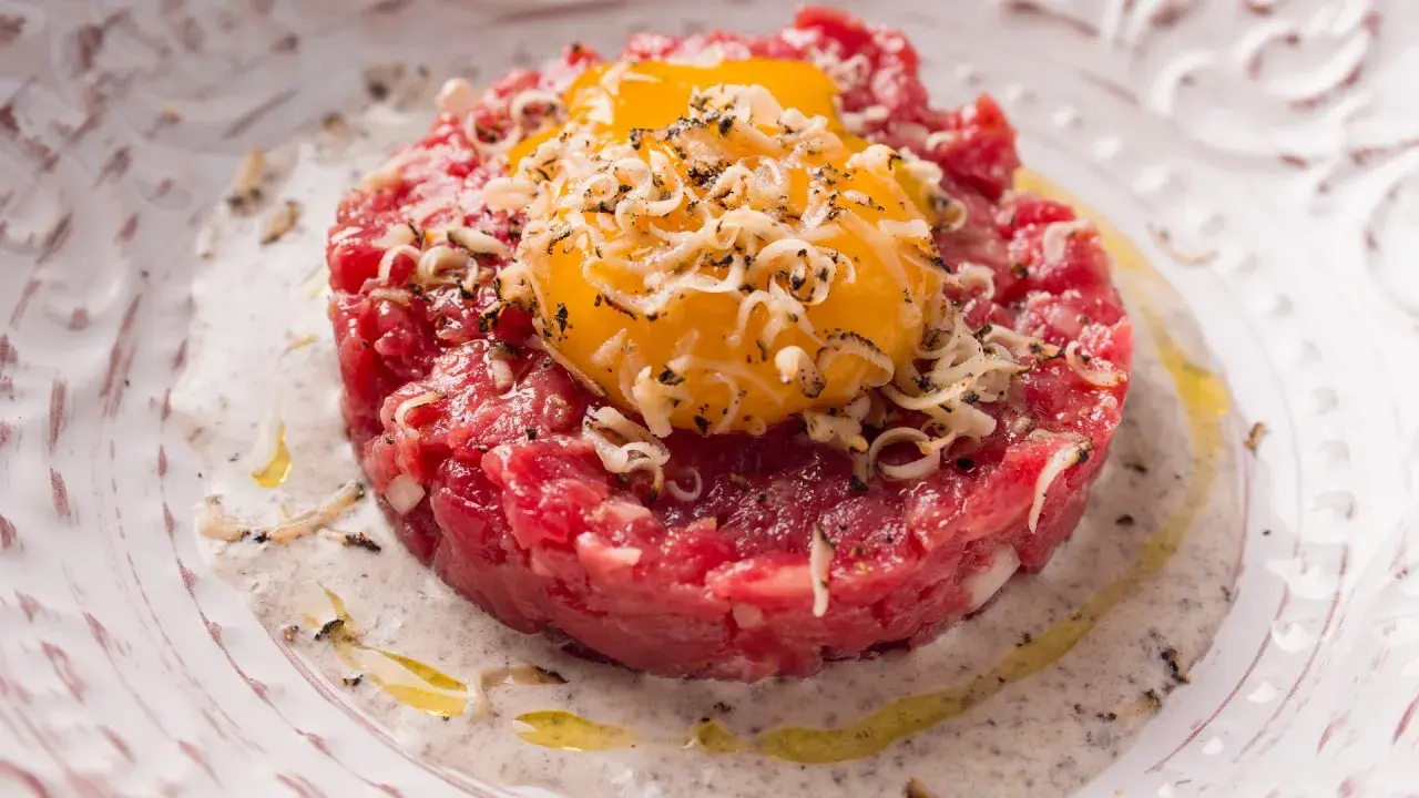 Tartare di manzo con tuorli d'uovo, cipolla e formaggio grattugiato. Un'idea su come condirla per un piatto gourmet.