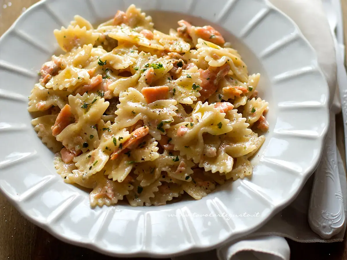 Farfalle cremose con salmone affumicato, un piatto delizioso e invitante, guarnito con prezzemolo fresco e pepe nero.
