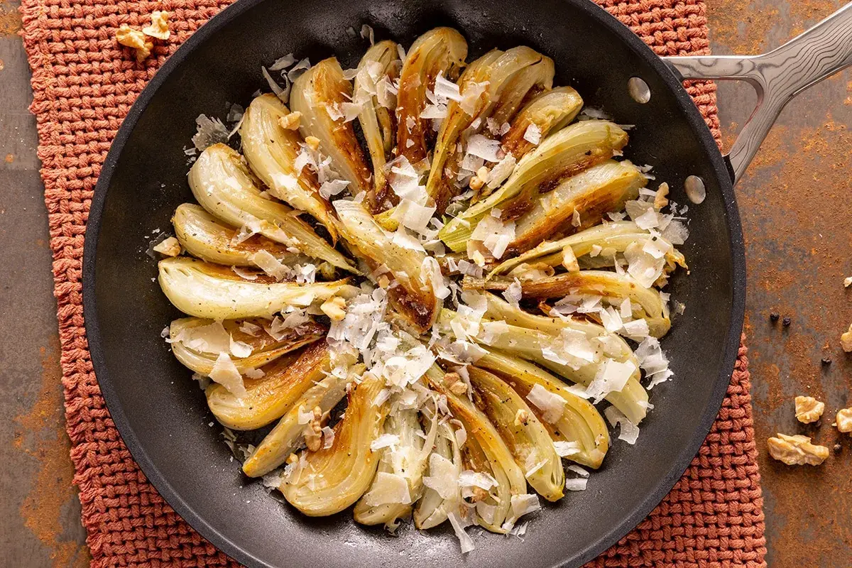 Finocchi in padella dorati, guarniti con scaglie di formaggio e noci croccanti. Un piatto semplice e saporito.