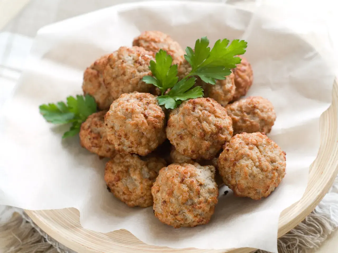 Un mucchio di polpette di pollo dorate e profumate, guarnite con prezzemolo fresco, servite su carta da forno in un piatto di legno.
