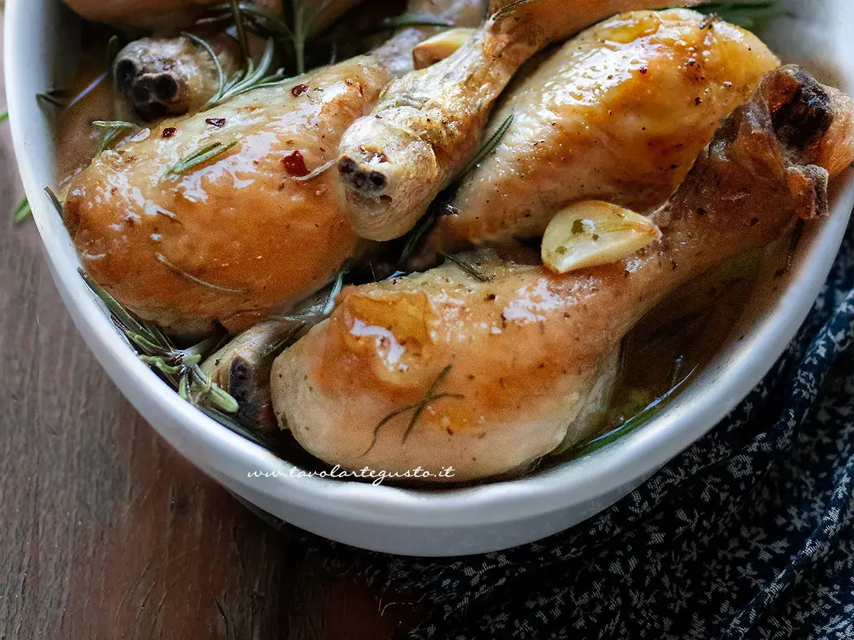 Cosce di pollo al forno succulente, dorate e profumate al rosmarino e aglio, servite in una ciotola bianca.
