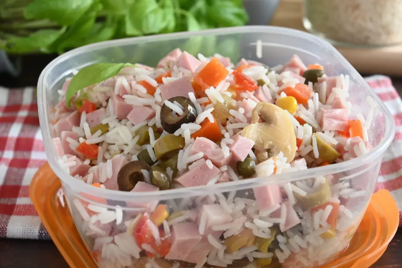 Insalata di riso colorata con prosciutto a cubetti, carote, olive, piselli e funghi, pronta per un pasto veloce.