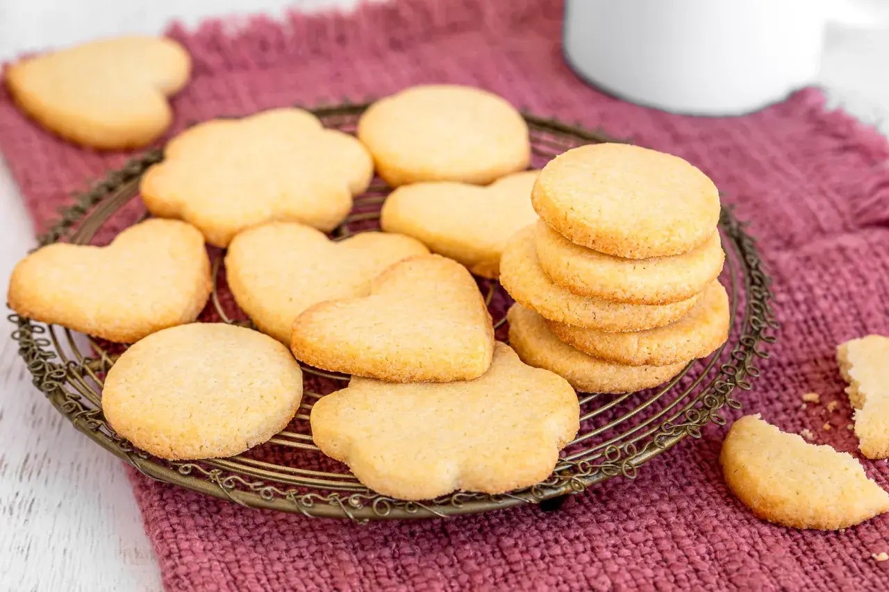 Deliziosi dolci da fare in casa: biscotti a forma di cuore e fiori su una gratella, con una pila di biscotti rotondi e un pezzo rotto in primo piano.