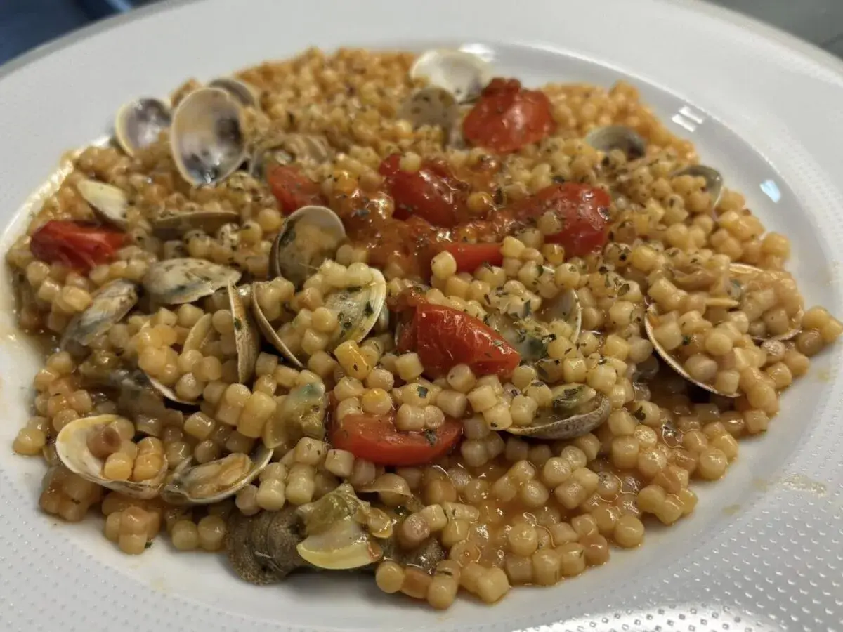 Un piatto invitante di fregola con vongole, pomodorini e prezzemolo, pronto per essere gustato.