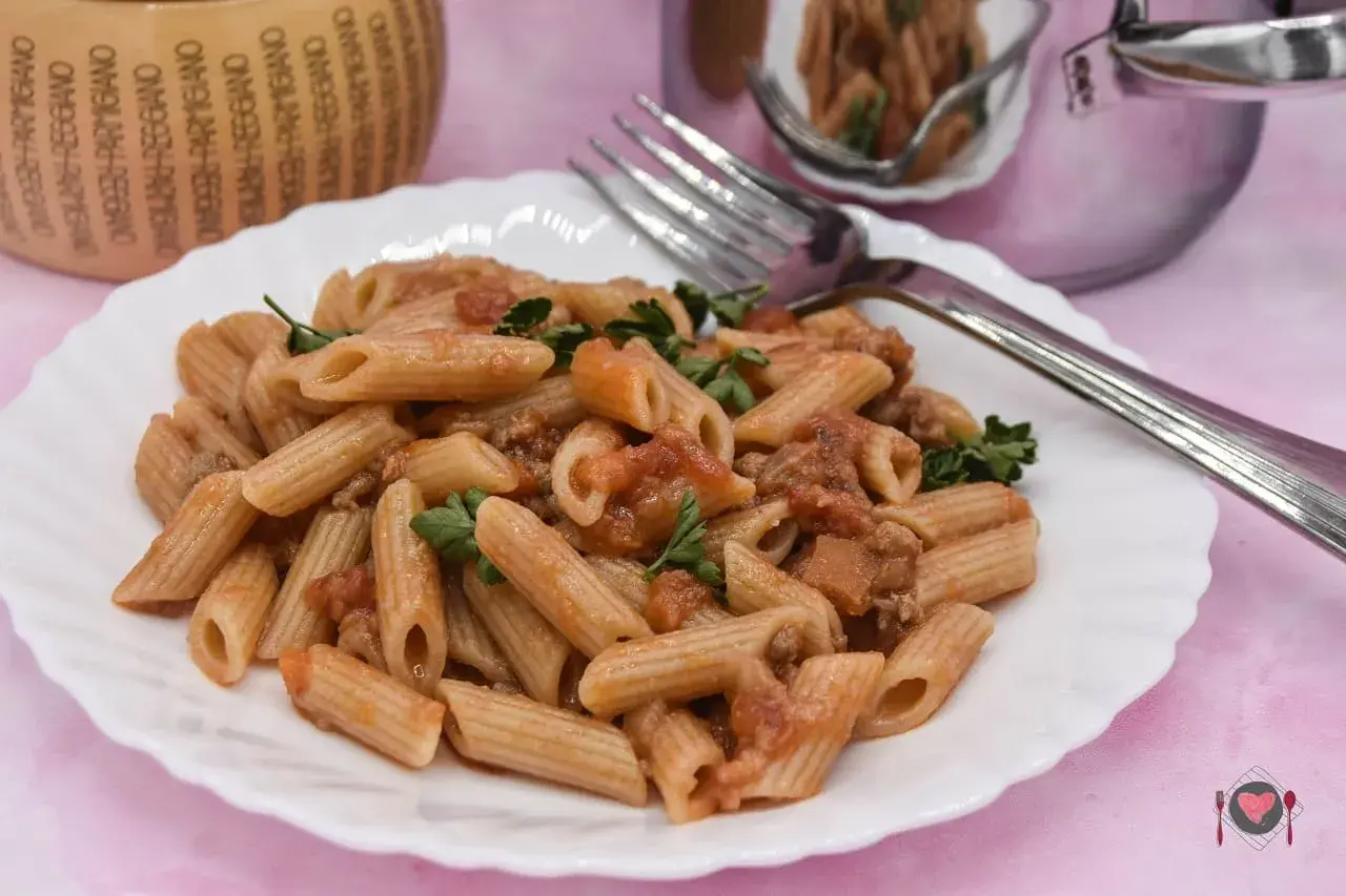 Piatto di pasta con salsiccia e pomodoro, guarnito con prezzemolo fresco. Un classico della cucina italiana, pronto per essere gustato.
