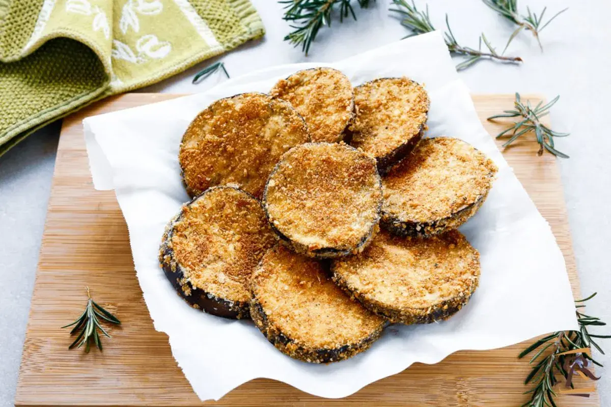 Cotolette di melanzane dorate e croccanti, servite su carta bianca con rametti di rosmarino.