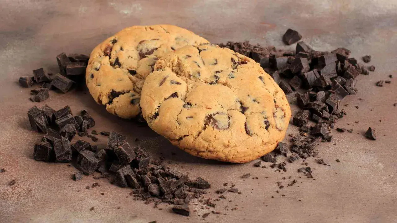 Due golosi cookies con gocce di cioccolato, perfetti per la tua ricetta crumble cookies, circondati da pezzetti di cioccolato fondente.