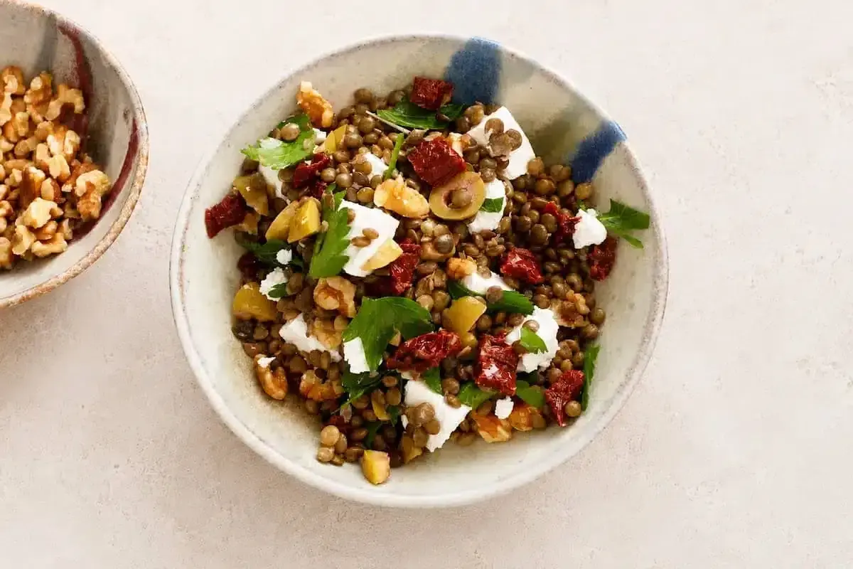 Insalata di lenticchie estiva con feta, pomodori secchi, olive e noci. Fresca e saporita, perfetta per un pasto leggero.