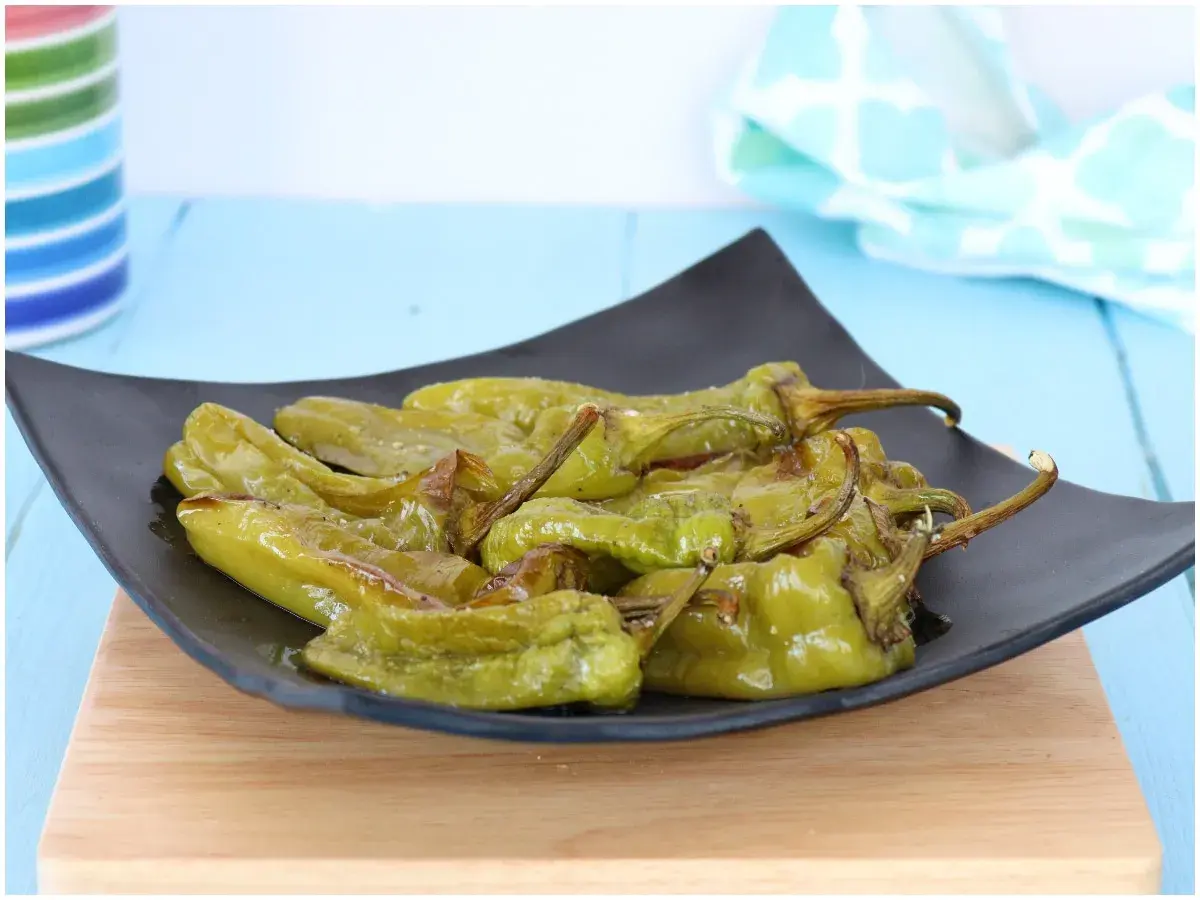 Friggitelli al forno, verdi e lucidi, serviti su un piatto nero. Un contorno saporito e facile da preparare.