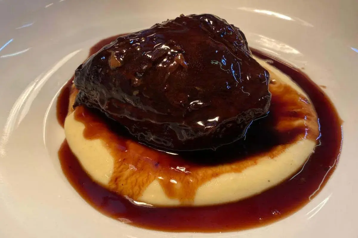 Guancia di manzo brasata, tenerissima e succulenta, adagiata su un letto di purè cremoso, il tutto avvolto da una ricca salsa scura.
