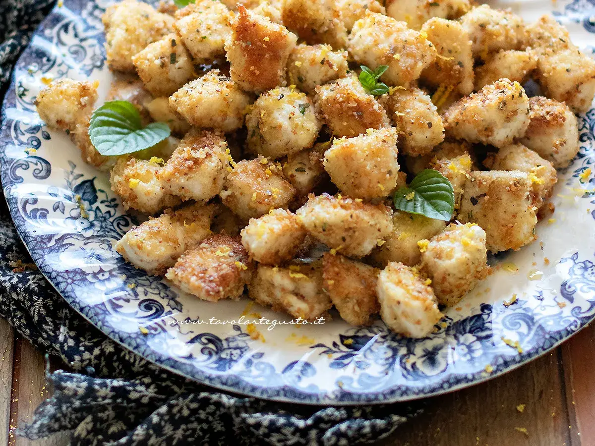 Croccante spezzatino di pollo impanato, guarnito con scorza di limone e menta fresca, servito su un piatto decorato.