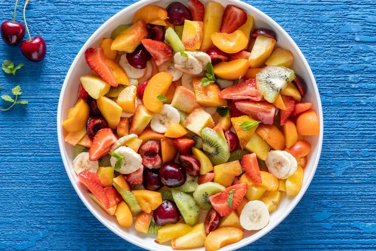 Una colorata macedonia di frutta fresca, con fragole, kiwi, pesche, banane e ciliegie, pronta per essere gustata.