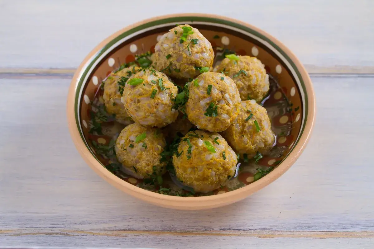 Polpette di riso avanzato, dorate e profumate, servite in una ciotola decorata, con erbe fresche tritate.