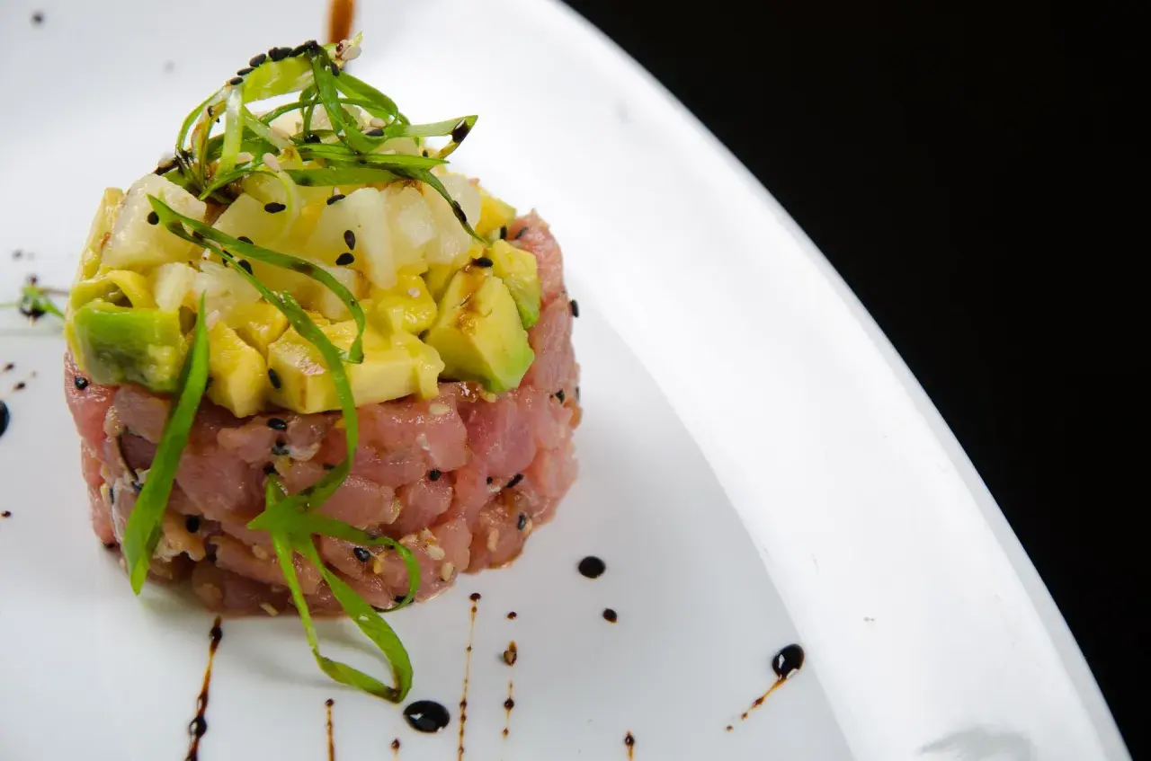 Deliziosa tartare di tonno con avocado, ananas e cipollotto fresco, guarnita con semi di sesamo e un filo di salsa.