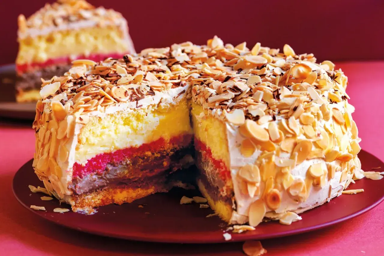 Una fetta di pizza dolce abruzzese, con strati di crema, cioccolato e confettura, ricoperta di mandorle tostate e scaglie di cioccolato.