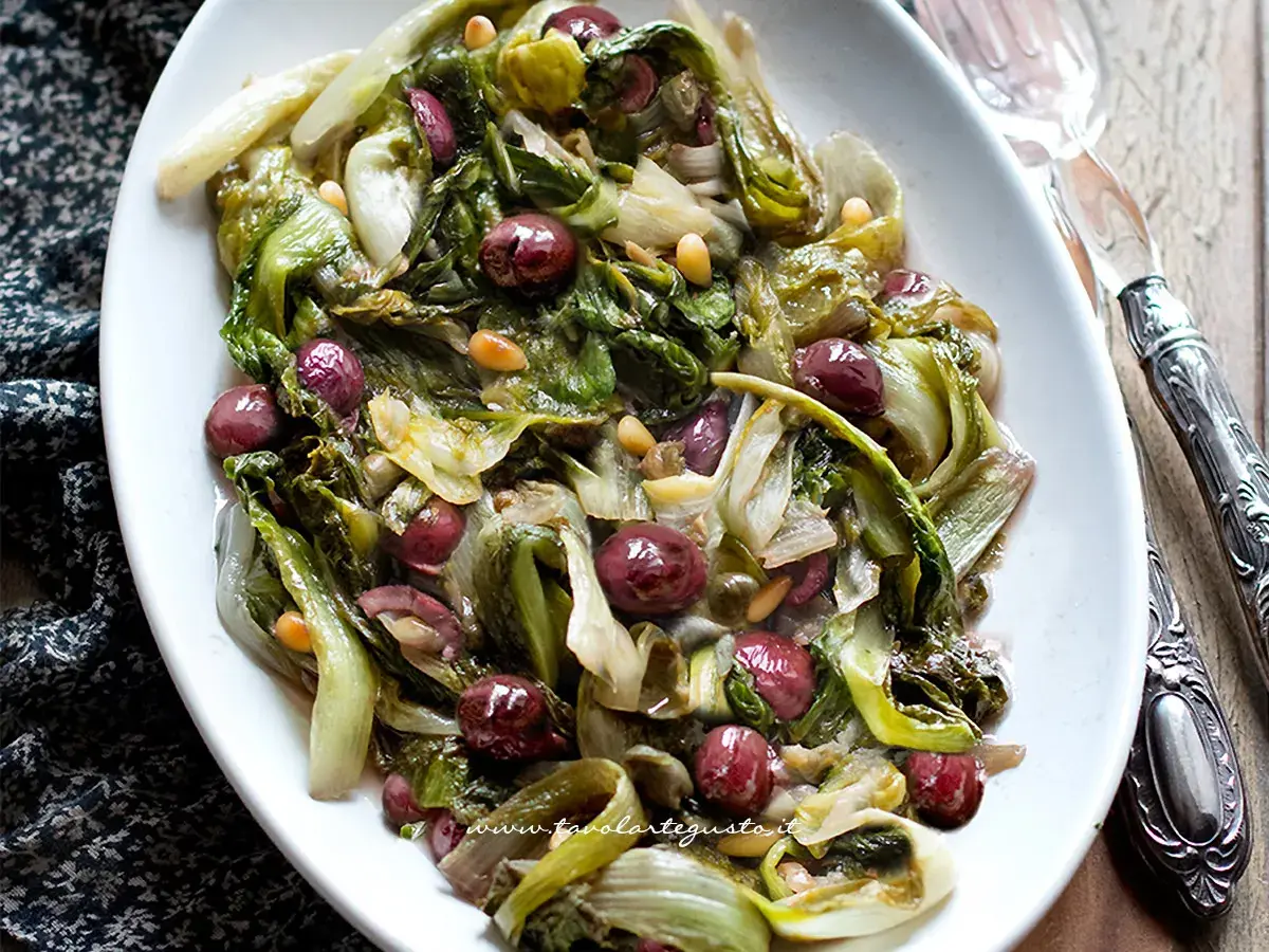 Scarola in padella con olive nere e pinoli, un contorno saporito e colorato, pronto per essere gustato.