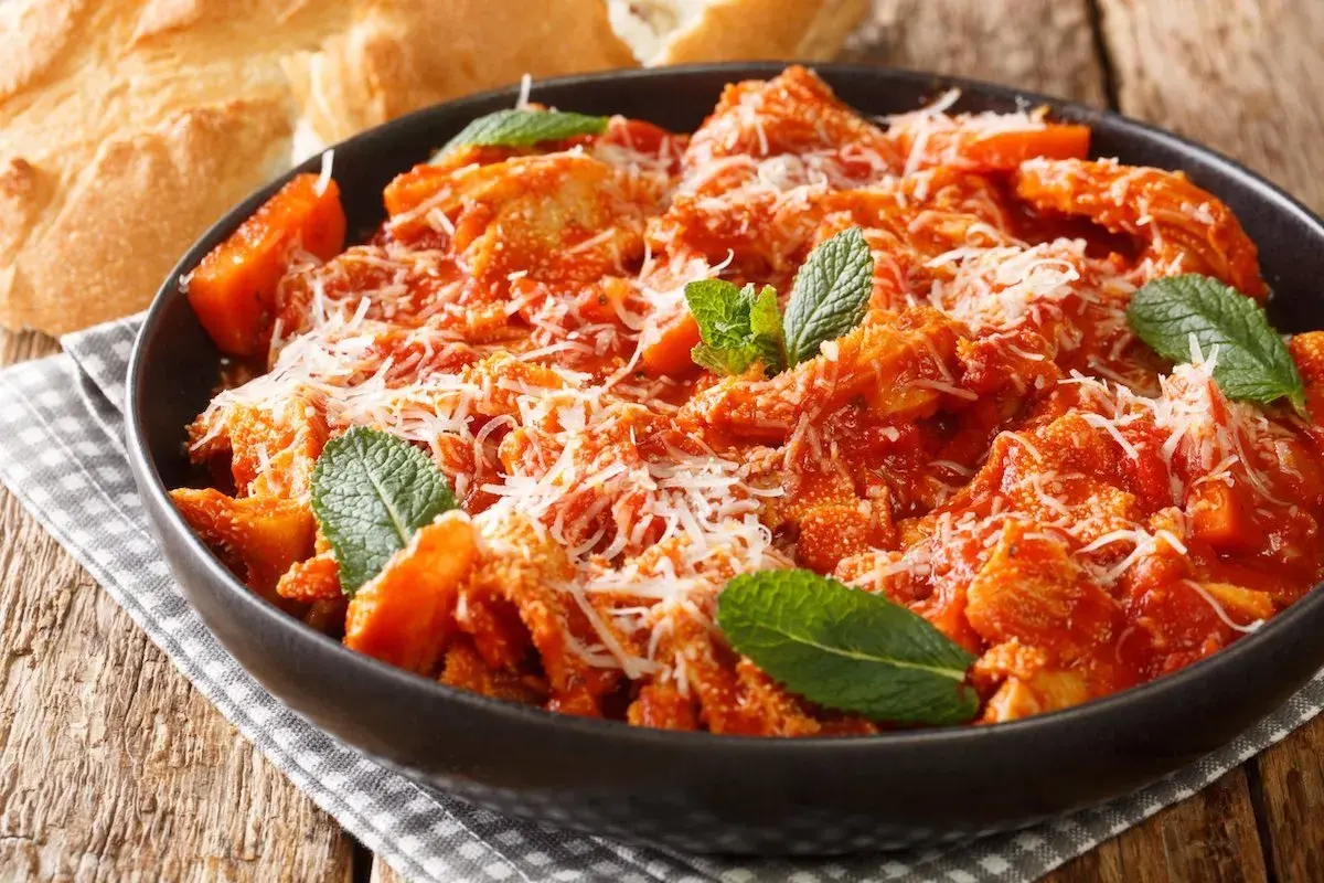 Trippa alla romana, la ricetta della nonna, servita in una ciotola scura con parmigiano e menta. Accanto, pane casereccio.