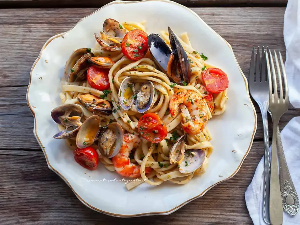Un piatto invitante di scialatielli ai frutti di mare, con cozze, vongole e gamberi, guarnito con pomodorini e prezzemolo.
