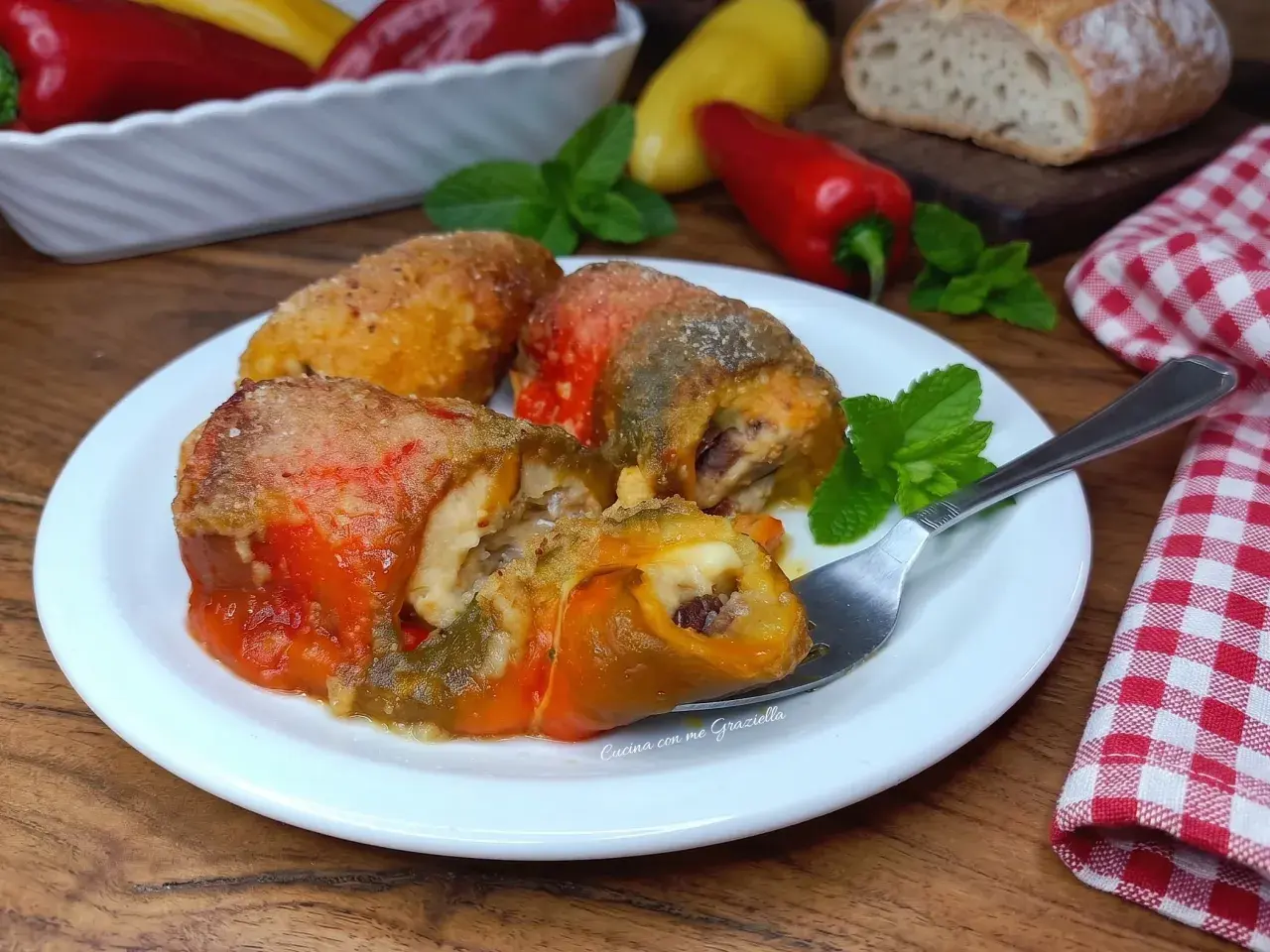 Deliziosi involtini di peperoni ripieni, dorati e succulenti, serviti su un piatto bianco con menta fresca.