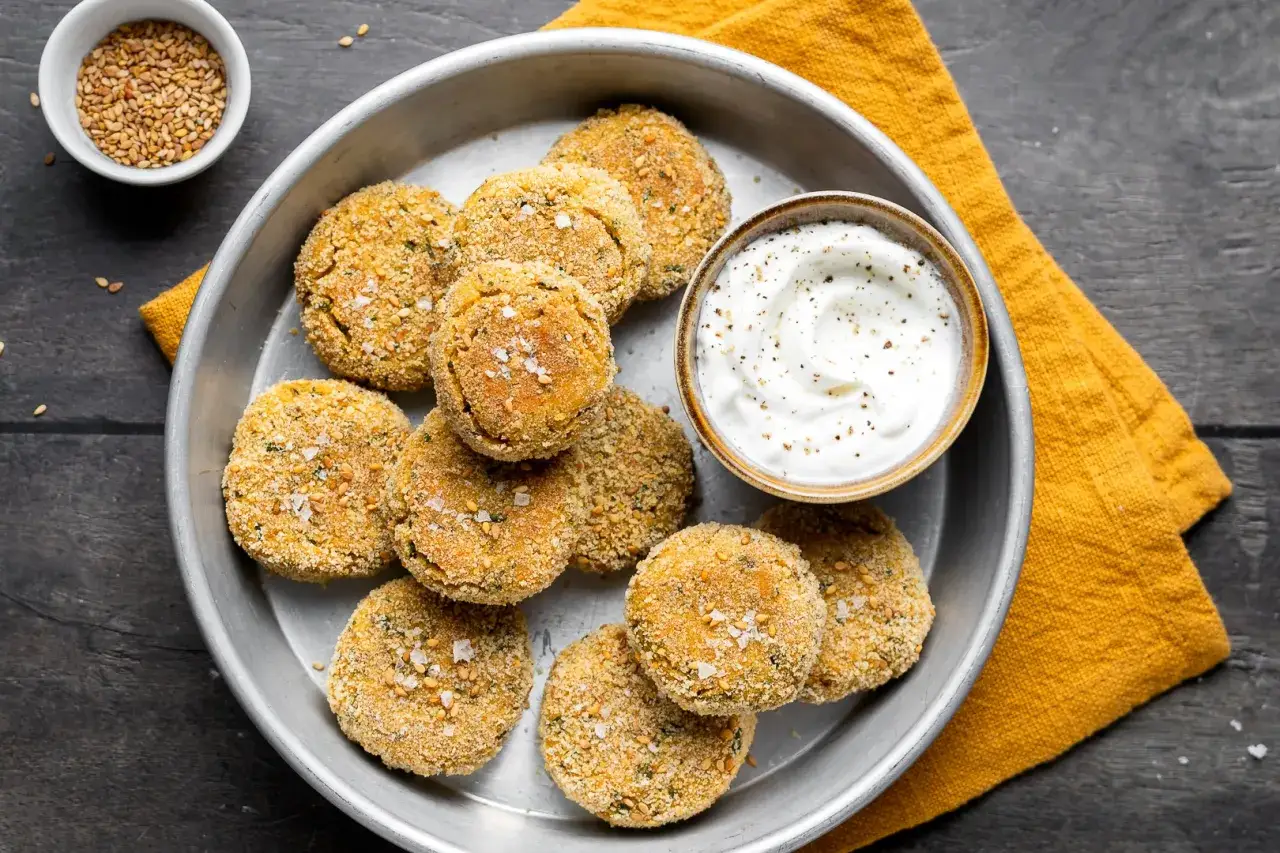 Deliziose polpette di ceci dorate e croccanti, servite su un piatto d'argento con una ciotola di salsa cremosa e un tovagliolo giallo.
