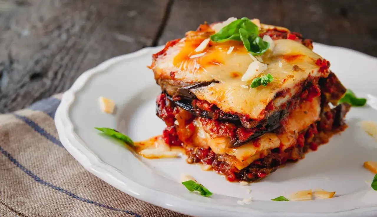 Una fetta di parmigiana di melanzane ricetta originale, con strati di melanzane, sugo e formaggio filante, guarnita con basilico fresco.