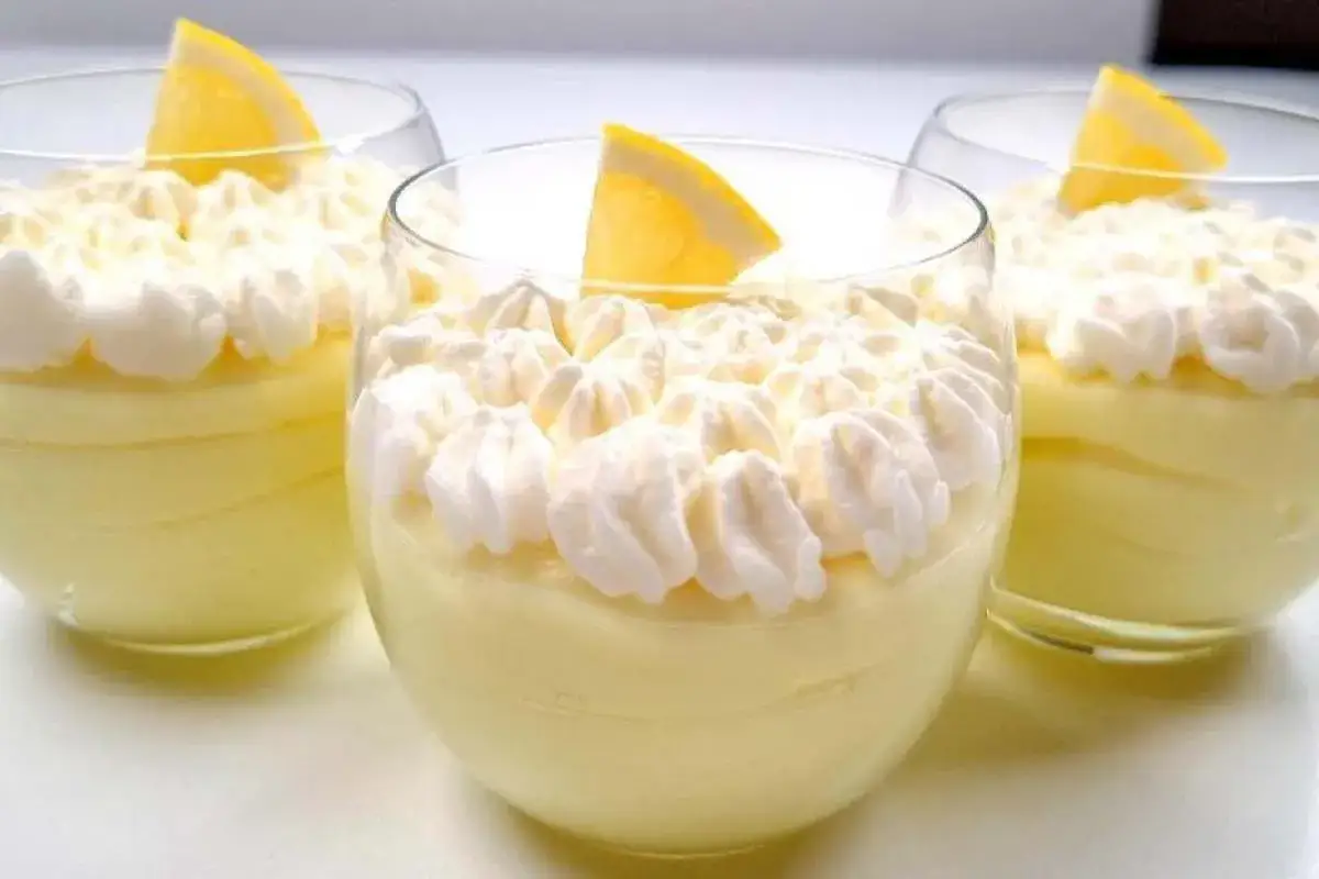 Tre bicchieri di deliziosa mousse al limone, guarniti con panna montata e una fetta di limone.
