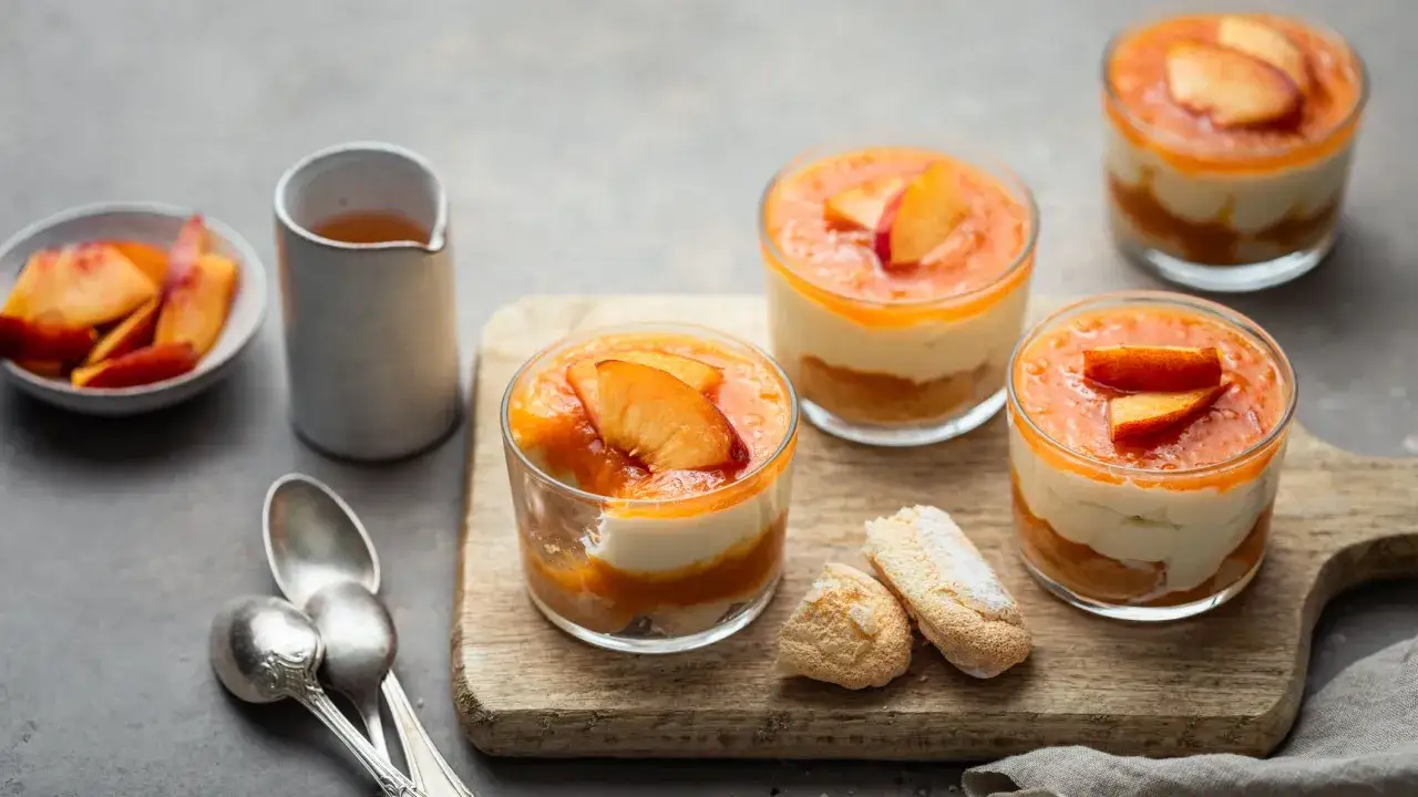 Delizioso tiramisù alle pesche in coppette, guarnito con pesche fresche e accompagnato da savoiardi.