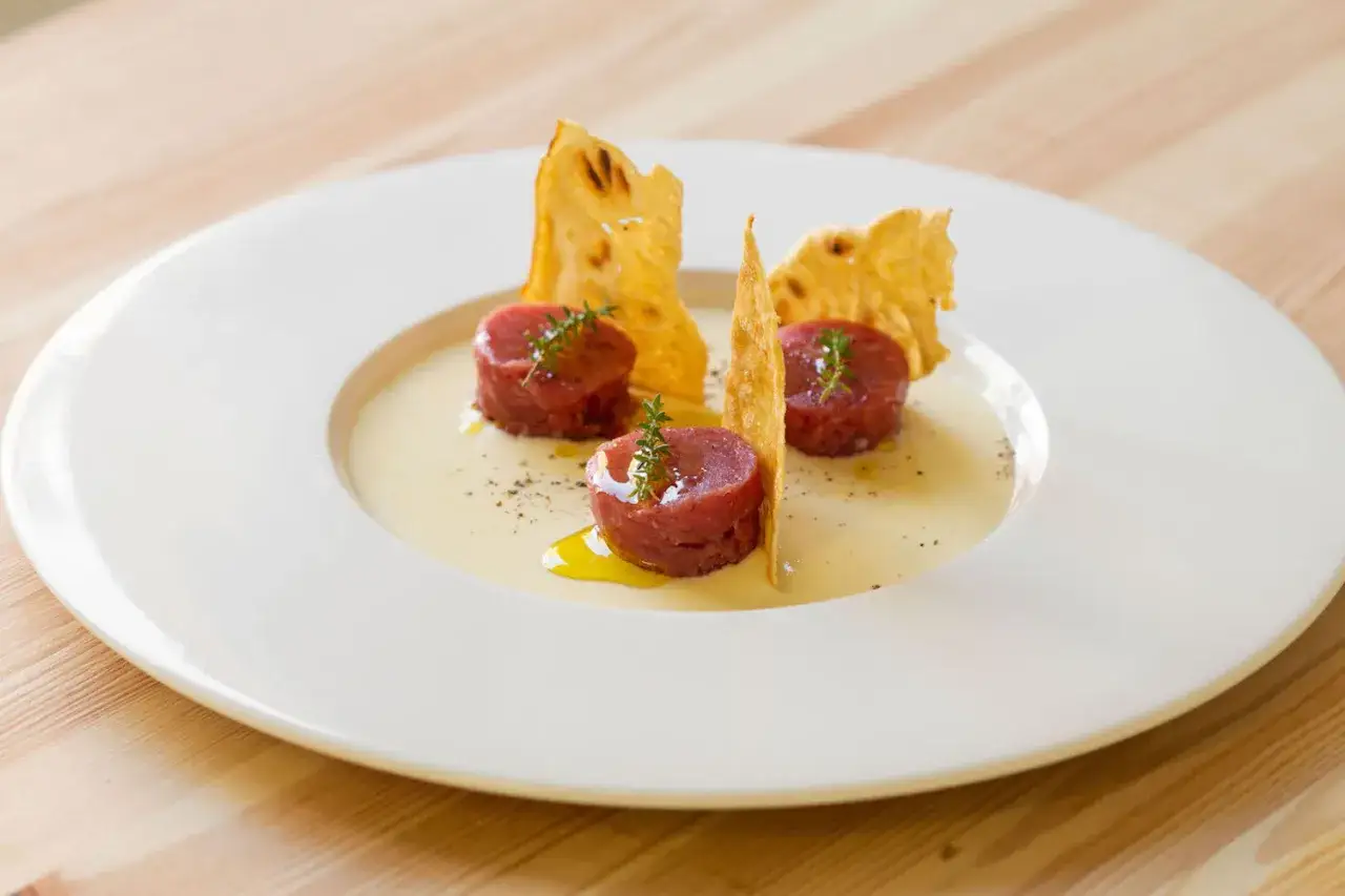 Deliziosa tartare di manzo, servita su una crema chiara con croccanti cialde e un rametto di timo.