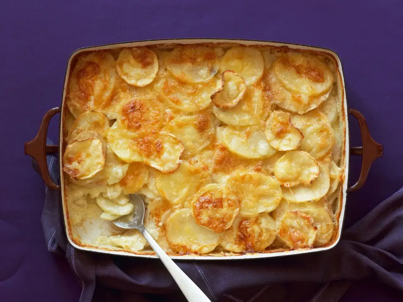 Parmigiana di patate dorata e cremosa, appena sfornata, con una fetta servita.