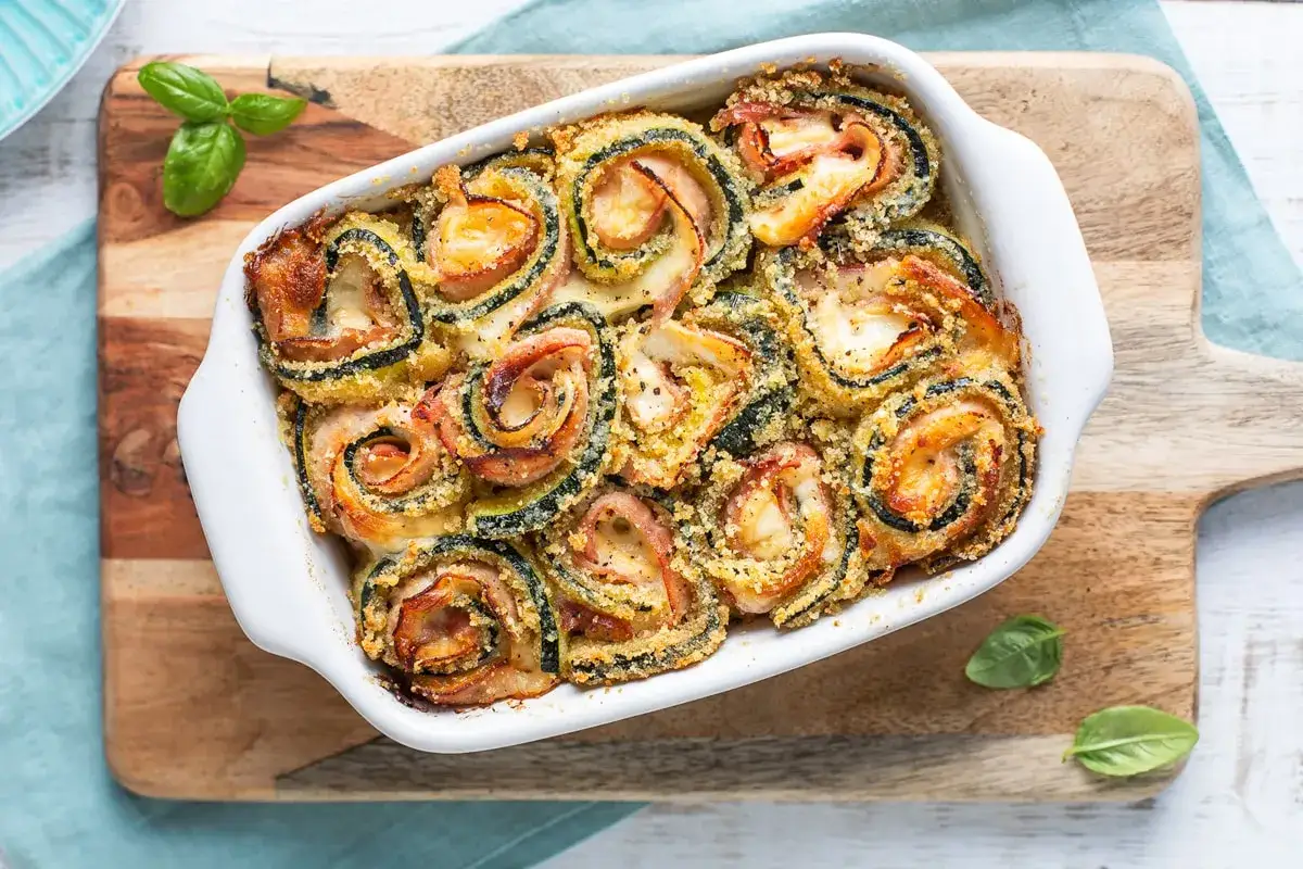 Involtini di zucchine al forno, dorati e filanti, con prosciutto e formaggio. Un piatto gustoso e leggero.