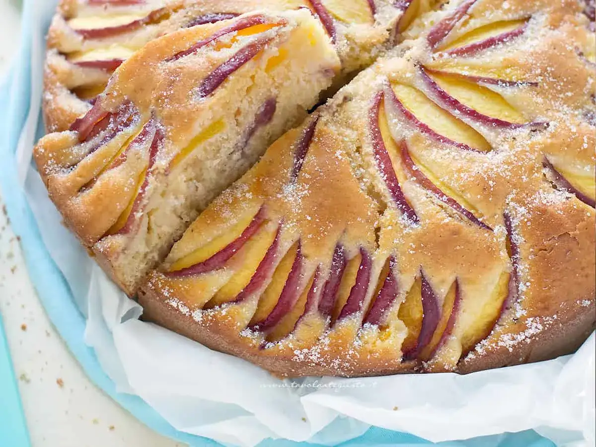 Una deliziosa torta di pesche, con fette di frutta disposte a raggiera sulla superficie dorata e cosparsa di zucchero.