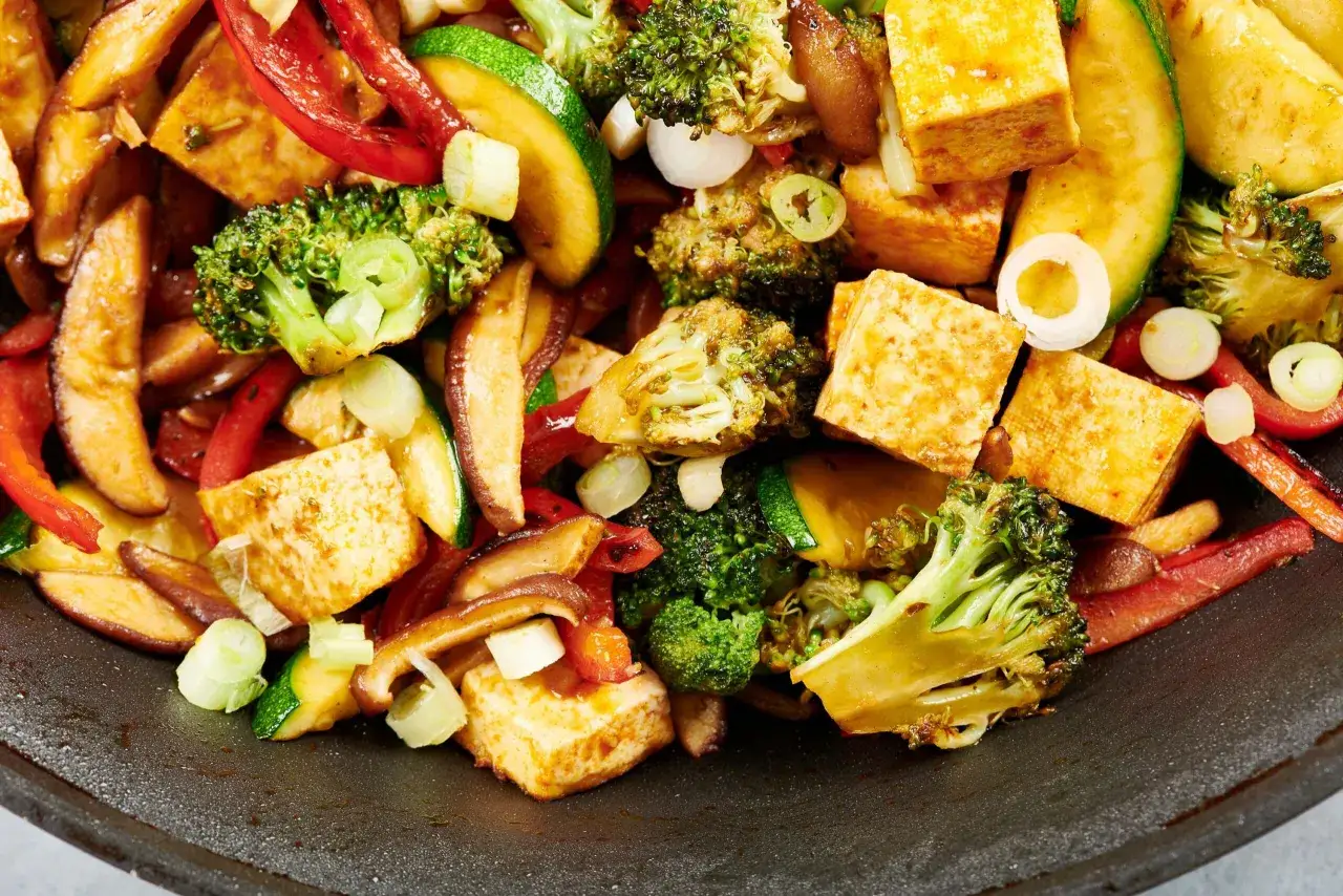 Tofu in padella con broccoli, peperoni rossi, zucchine e funghi. Un piatto colorato e saporito, pronto per essere gustato.