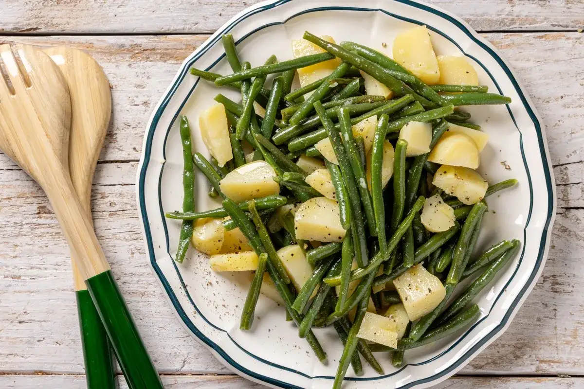 Un piatto di fagiolini e patate conditi, pronti per essere serviti con le posate in legno.