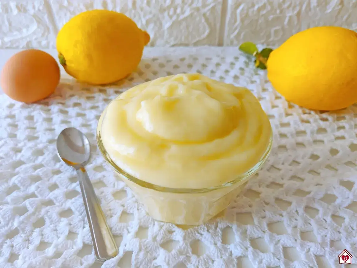 Una ciotola di deliziosa crema al limone, pronta per essere gustata. Accanto, un uovo e limoni freschi, ingredienti chiave per questa bontà.