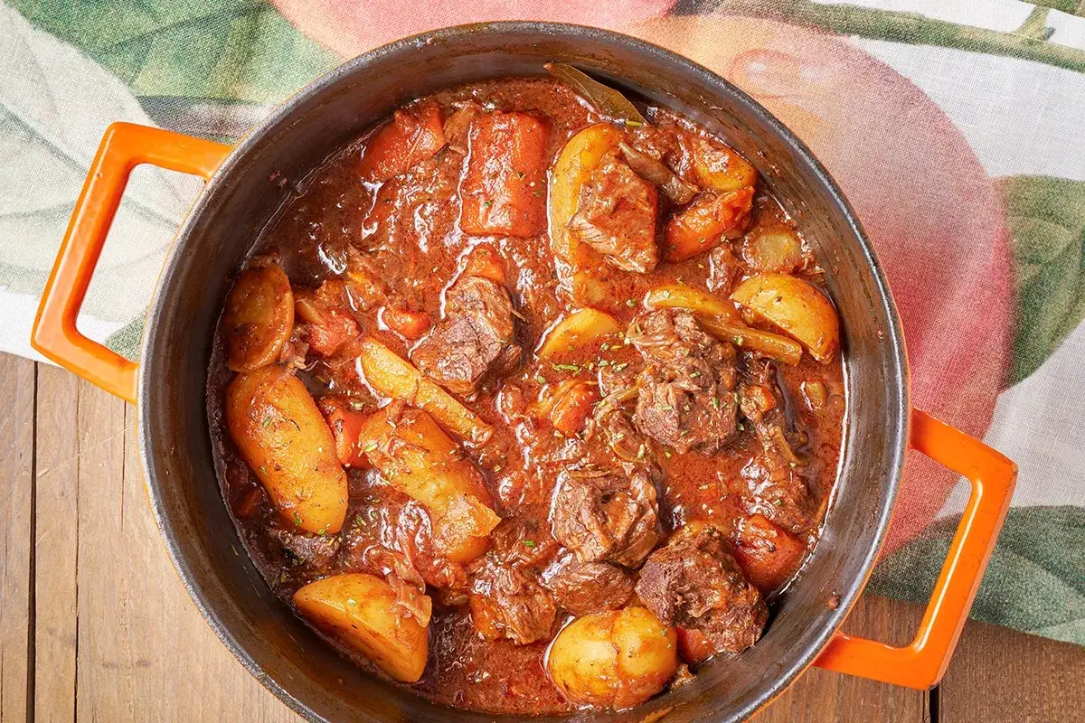 Un saporito spezzatino di vitello con patate e carote in un tegame di ghisa arancione, pronto per essere gustato.