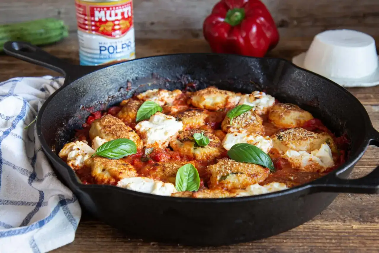 Polpette di pollo al forno con pomodoro e ricotta, guarnite con basilico fresco. Un piatto invitante e saporito.